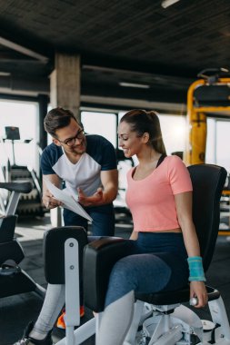 Modern spor salonunda spor yapan genç ve çekici bir kadın. Kişisel fitness hocası veya koçuyla birlikte..