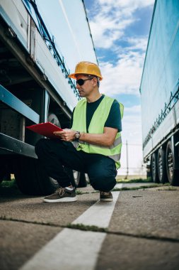 Sarı kasklı profesyonel sanayi kamyonu şoförü bir sonraki sürüşten önce aracın teknik denetimini yapıyor..