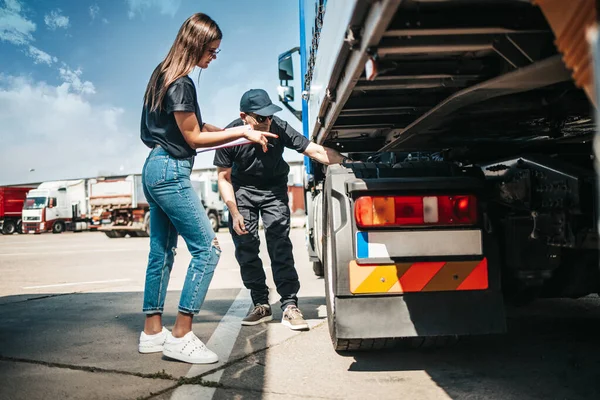 Two professional truck drivers stand in front of the big truck. They talk and perform a technical inspection of the vehicle before next drive. Professional transportation concept.