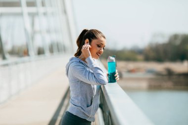 Güzel, genç ve formda bir kadın şehir köprüsü caddesinde koştuktan ve koştuktan sonra rahatlıyor. Spor kulaklık takıyor ve müzik dinliyor..