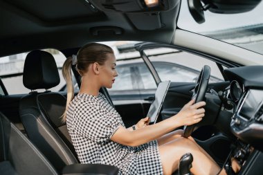 Kullanılmış araba satıcısı olarak çalışan güzel bir genç kadın. Müşteri veya alıcıdan önce dijital tablet kullanıyor ve araba durumunu kontrol ediyor. Kullanılmış araç galerisi.