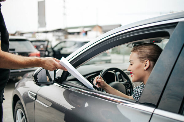 Satisfied and smiled female buyer sitting in her new car. She happy while signing buyer's purchase contract with used car seller.