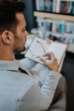 Orta yaşlı bir adam modern kitapçıda kitap seçiyor ve okuyor..