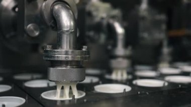 Modern bir mandıra fabrikasındaki endüstriyel bir taşıma bandında plastik bardakları kremalı yoğurtla dolduran robot makine, otomatikleştirilmiş gıda üretim sürecini yakın plandan gösteriyor.