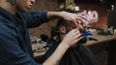 Profesyonel berber bir adamın saçını ustura ile kesiyor ve geleneksel bir berber dükkanında saç çizgisini şekillendiriyor. Bakım aletleriyle temiz ve keskin bir görünüm sağlıyor.