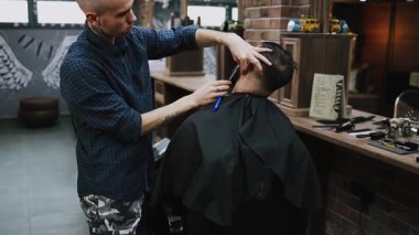 Profesyonel berber bir adamın saçını ustura ile kesiyor ve geleneksel bir berber dükkanında saç çizgisini şekillendiriyor. Bakım aletleriyle temiz ve keskin bir görünüm sağlıyor.