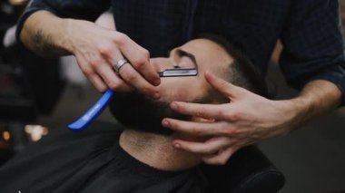 Profesyonel berber bir adamın saçını ustura ile kesiyor ve geleneksel bir berber dükkanında saç çizgisini şekillendiriyor. Bakım aletleriyle temiz ve keskin bir görünüm sağlıyor.