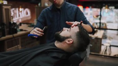 Profesyonel berber bir adamın saçını ustura ile kesiyor ve geleneksel bir berber dükkanında saç çizgisini şekillendiriyor. Bakım aletleriyle temiz ve keskin bir görünüm sağlıyor.