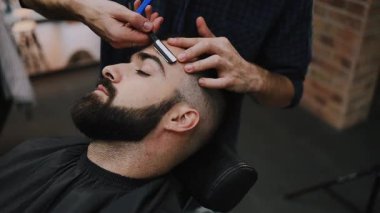 Profesyonel berber bir adamın saçını ustura ile kesiyor ve geleneksel bir berber dükkanında saç çizgisini şekillendiriyor. Bakım aletleriyle temiz ve keskin bir görünüm sağlıyor.