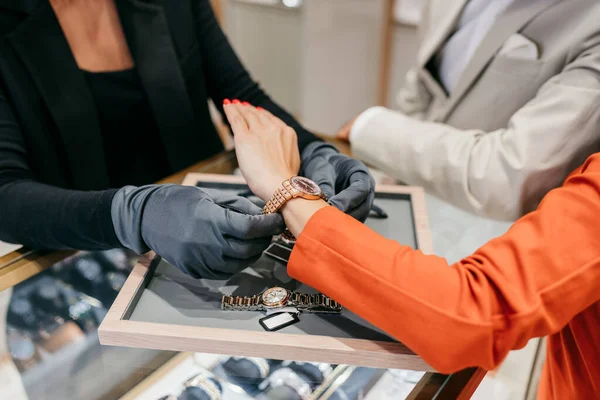 Özel perakende hizmeti sunan lüks bir kuyumcuda şık bir kol saati deneyen müşteriye koruyucu eldivenler satan bir satış elemanı.