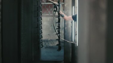 Solunum maskesi takan profesyonel bir erkek işçi. Endüstriyel sprey kabinindeki bir konveyör hattından sarkan metal parçalarına toz kaplaması uygulamak için sprey tabanca kullanıyor.