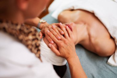 Profesyonel güzellik uzmanı masaj masasında uzanan kadın müşteriye nazikçe masaj yapıyor. Rahatlatıcı ve gençleştirici cilt bakımı sağlıyor.