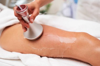 Uzman bir cihaz kullanan profesyonel güzellik uzmanı modern bir kaplıca veya güzellik salonunda bir kadının kalçasına anti-selülit tedavisi uygulayıp pürüzsüz ve renkli bir cilt garantisi veriyor.