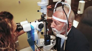 Üst düzey bir erkek hastanın gözlerini modern kliniğinde bir yarık lambasıyla inceleyen kadın göz doktoru görüşünü dikkatlice kontrol ediyor ve olası göz hastalıklarını teşhis ediyor.
