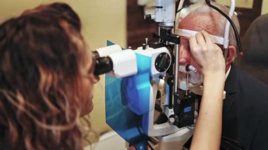 Üst düzey bir erkek hastanın gözlerini modern kliniğinde bir yarık lambasıyla inceleyen kadın göz doktoru görüşünü dikkatlice kontrol ediyor ve olası göz hastalıklarını teşhis ediyor.