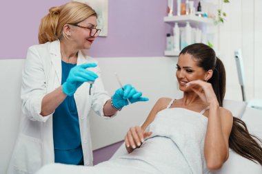 Güzellik kliniğindeki güzel ve mutlu esmer kadın. Kadın doktorla yüz estetiği hakkında konuşuyor..