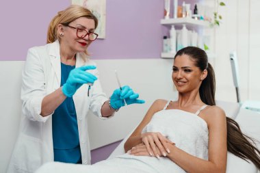 Güzellik kliniğindeki güzel ve mutlu esmer kadın. Kadın doktorla yüz estetiği hakkında konuşuyor..