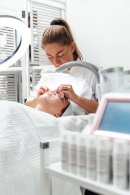 Profesyonel güzellik uzmanı, yüz estetiği ameliyatı sırasında kağıt mendille tedavi masasında yatan genç bir kadının burnundaki sivilceyi çıkarıyor.