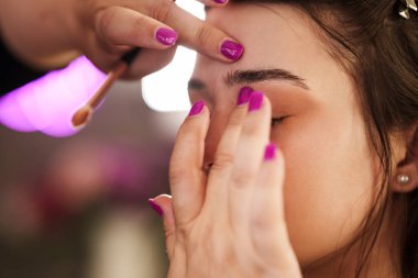 Profesyonel güzellik uzmanı güzel genç bir kadının yüzüne makyaj yapıyor. Muhteşem bir kadın modelle profesyonel makyaj stüdyosu çalışması..