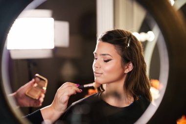 Profesyonel güzellik uzmanı güzel genç bir kadının yüzüne makyaj yapıyor. Muhteşem bir kadın modelle profesyonel makyaj stüdyosu çalışması..