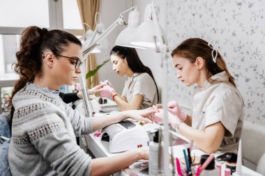 Modern bir güzellik salonunda çalışan profesyonel manikürcüler. Tatmin olmuş kadın müşteriler kaplıca merkezinde manikür tedavisi görüyor..