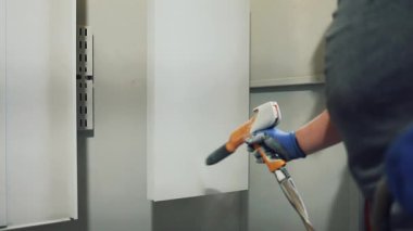 Solunum maskesi takan profesyonel bir erkek işçi. Endüstriyel sprey kabinindeki bir konveyör hattından sarkan metal parçalarına toz kaplaması uygulamak için sprey tabanca kullanıyor.