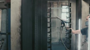 Solunum maskesi takan profesyonel bir erkek işçi. Endüstriyel sprey kabinindeki bir konveyör hattından sarkan metal parçalarına toz kaplaması uygulamak için sprey tabanca kullanıyor.