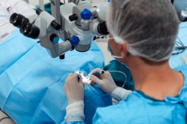 Profesyonel cerrah mikro-invazif göz prosedürünü cerrahi mikroskop ve modern klinik ortamında mavi steril perdeler kullanarak gerçekleştiriyor..