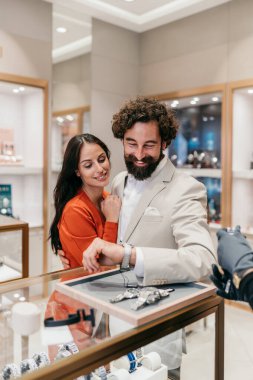 Sofistike bir çift gülümserken adam kuyumcu tezgahında pahalı bir kol saatini denerken profesyonel bir satış elemanı da ona yardım ediyor..