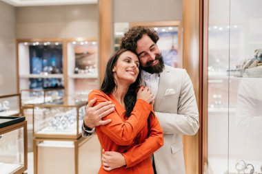 Romantik, zarif bir çift lüks bir mağaza veya galeride pahalı saatlere ve mücevherlere bakarken sevgi dolu bir kucaklaşmayı paylaşıyor..