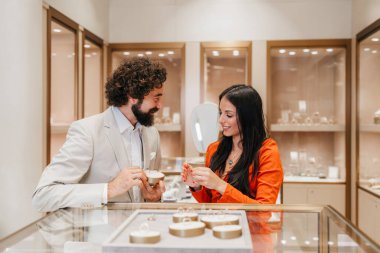 Üst düzey bir mücevher mağazasında yüzüklere bakıp evlilik teklifi ya da yıldönümü hediyesi alma ihtimalini tartışan mutlu bir çift gülümsüyor..