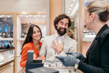 Mutlu bir çift lüks bir butikte birinci sınıf mücevher almak için alışveriş yaparken profesyonel bir satış görevlisi onlara zarif bir altın bilezik gösterir..