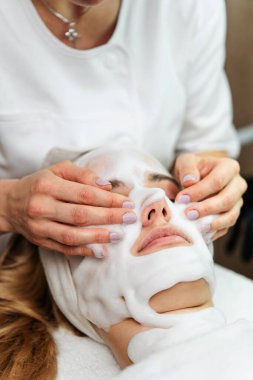 Profesyonel estetisyen, spa kliniğinde kadın bir müşteriye oksijen köpüğü kullanarak derin bir yüz tedavisi uyguluyor..