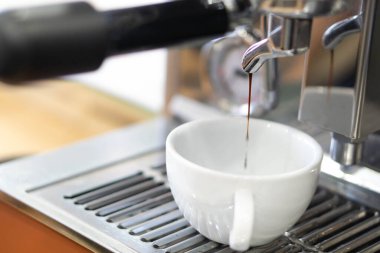 Kahve makinesinden beyaz fincana yakın espresso akıyor, seçici ve yumuşak odaklı.