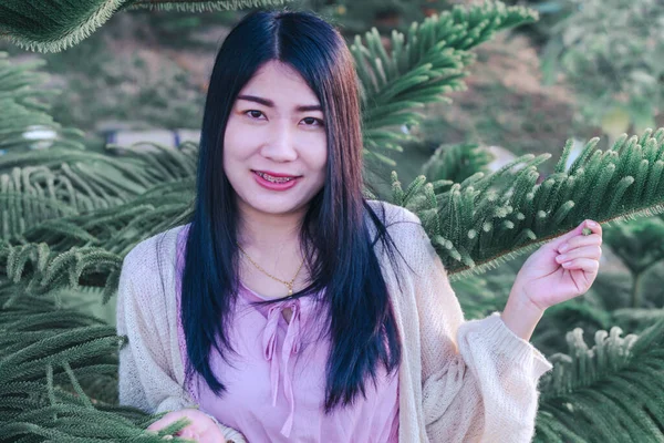 Portrait of asian happy woman smiling with Pine (Araucaria heterophylla) green leaves background.