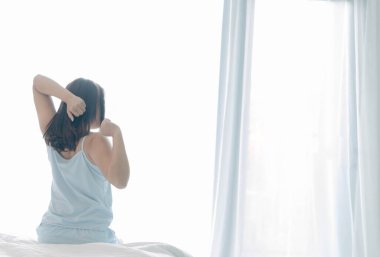 Kapalı kadın yatakta oturuyor ve sabah uyanıp dinlenmek için esniyor.