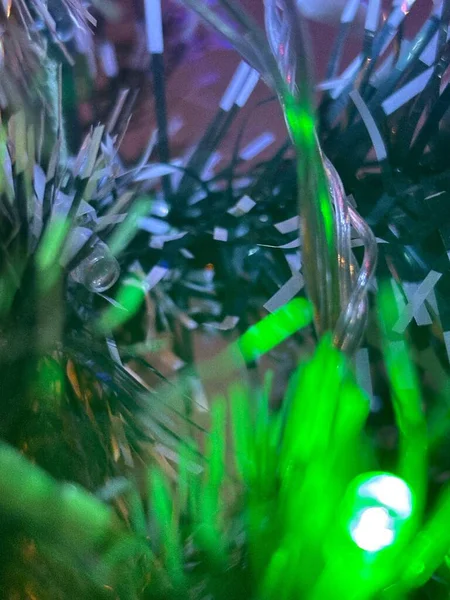 Renkli ışık iplikleri ve yeşil ve gümüş spot ışıklarıyla canlı bir Noel dekoru. Işıkların parıltısı büyülü, şenlikli bir atmosfer yaratıyor. Tatil ruhunu ve yıl sonu neşesini aktarmak için mükemmel..