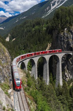 Parlak kırmızı bir tren ikonik Landwasser Viaduct boyunca zarif bir şekilde kıvrılır, bir mühendislik harikası ve muhteşem İsviçre Alpleri manzarasının ortasında Rhaetian Demiryolu 'nun en parlak noktası..
