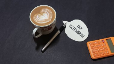 Vergi uzatma konsepti, bir fincan kahve hesap makinesi ve koyu renkli bir yüzey üzerindeki kalem finansal planlama ihtiyacını simgeliyor..