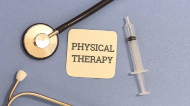 Stetoskop ve şırınga içeren fizik tedavi kavramı mavi bir yüzeyde üzerinde fizik tedavi yazan kartın yanında duruyor..