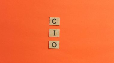 Cio kısaltmasını heceleyen tahta alfabe blokları parlak turuncu bir arkaplan ile dikey olarak ortalanmıştır..