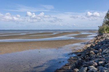 Avustralya 'nın Queensland kıyısındaki Moreton Körfezi kıyısındaki Beachmere' de mavi gökyüzü ve kümülüs bulut zeminine sahip kayalık bir kıyı duvarı ve kıyısı olan gelgitler arası geniş bir kum düzlüğü..