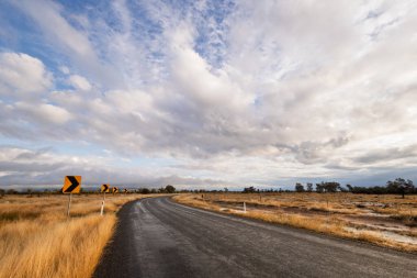 Güney Queensland, Avustralya 'da Yelarbon yakınlarındaki bu arazide bulut desenleri olan mavi gökyüzü altında bir zift ya da asfalt yol sağa doğru kıvrılır..