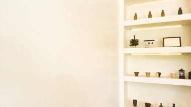 Basit çömlekler, küçük vazolar, çerçevelenmiş sanat eserleri, masa üstü takvimi ve küçük bir süs bitkisi ile dekore edilmiş parlak minimalist bir iç mekan. Sıcak ışıklandırma vurguları