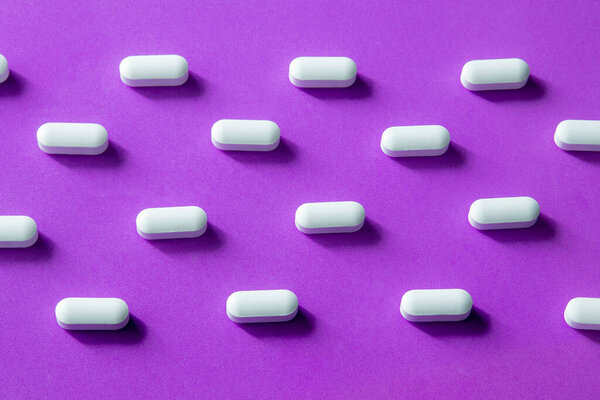 White pills arranged in geometric pattern on purple background. Modern concept of medicine, health care, pharmacy and design minimalism.