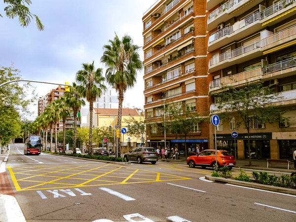 Barcelona. Spain. October 3, 2025. Urban street view with palm trees, apartment buildings, traffic, and people. A vibrant day in a residential neighborhood of the city.