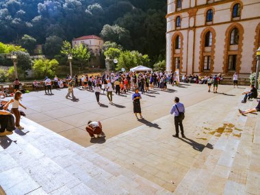 Barselona, İspanya. 3 Ekim 2025. Bir grup insan yeşil tepelerle çevrili tarihi bir binanın yakınındaki güneşli meydanda toplandı..