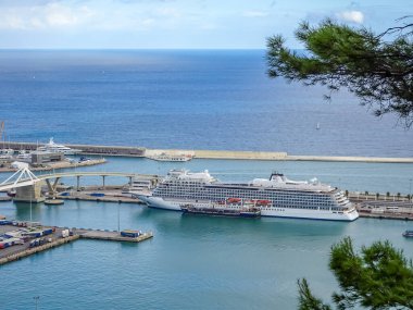 Barselona, İspanya. 5 Ekim 2025. Büyük beyaz bir yolcu gemisi Barcelona limanına yanaştı. Arkasında koyu mavi Akdeniz ve modern köprü vardı..