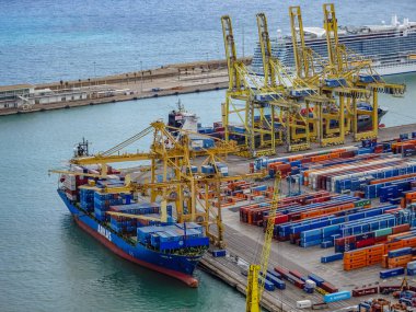 Barselona, İspanya. 5 Ekim 2025. Yükünü boşaltan vinçlerle limana yanaşmış büyük bir konteyner gemisi ARKAS. Meşgul liman terminaline istiflenmiş renkli konteynırlar.