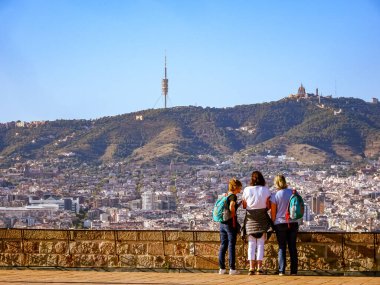 Güneşli bir günde Barselona 'nın panoramik manzarasının keyfini çıkaran turistler, Tibidabo tepesi ve arkada haberleşme kulesi bulunuyor. İspanya